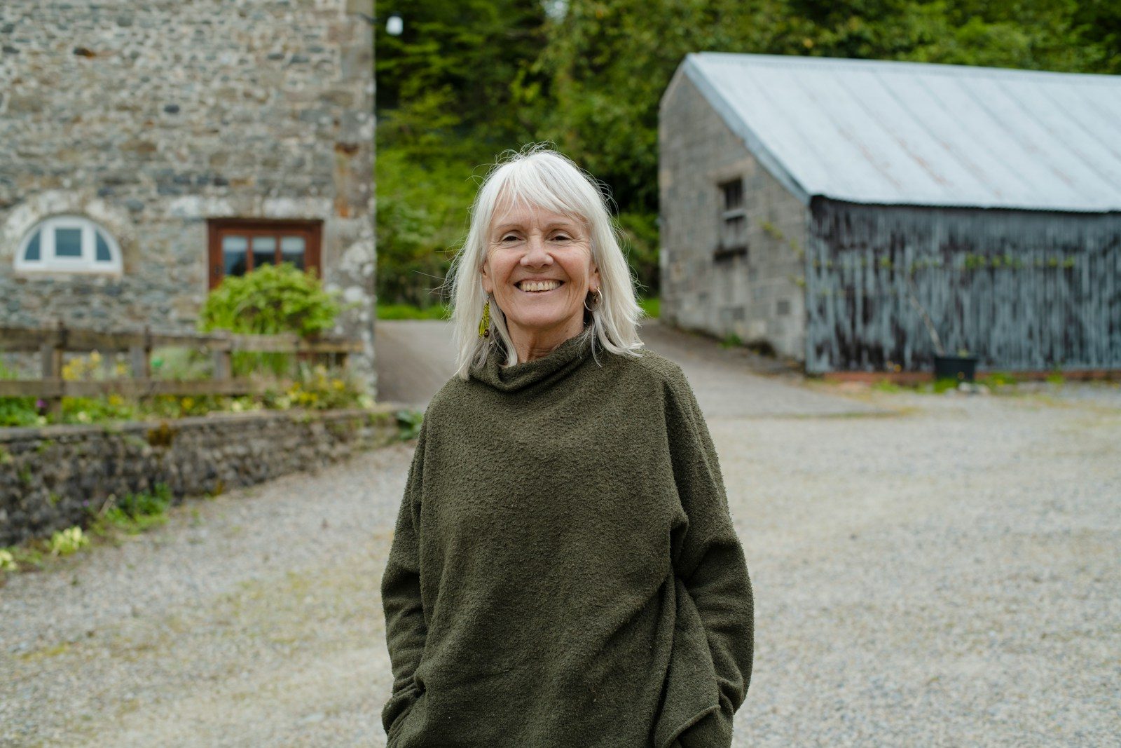 Smiling woman in green top stands outdoors near stone buildings.