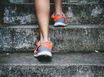 person wearing orange and gray Nike shoes walking on gray concrete stairs
