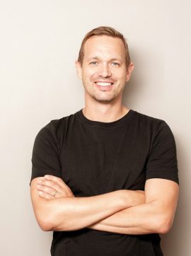 A smiling man with arms crossed on gray background