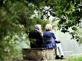 two people sitting on pavement facing on body of water